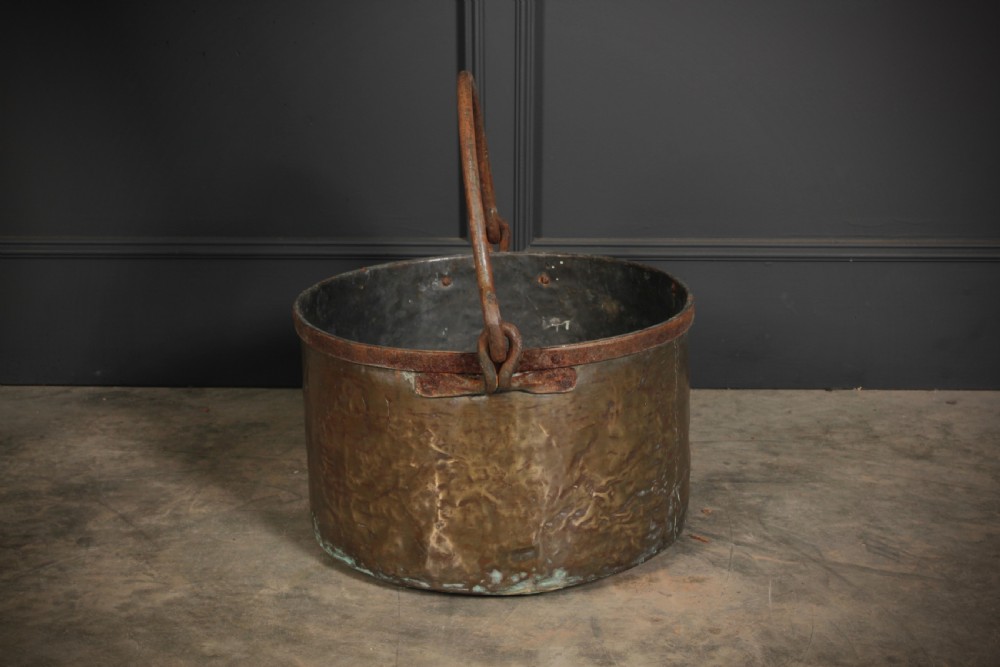 A large, hand-hammered Victorian brass cauldron featuring an iron rim collar and a heavy wrought iron swing handle. View V