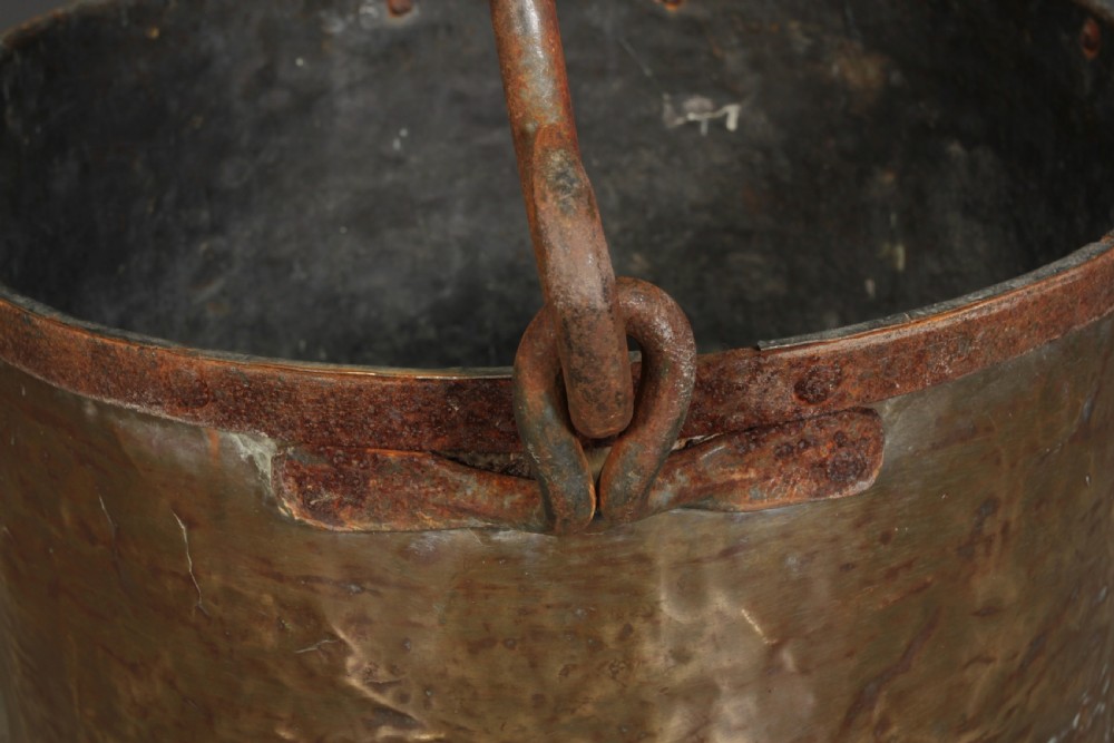 A large, hand-hammered Victorian brass cauldron featuring an iron rim collar and a heavy wrought iron swing handle. View VII