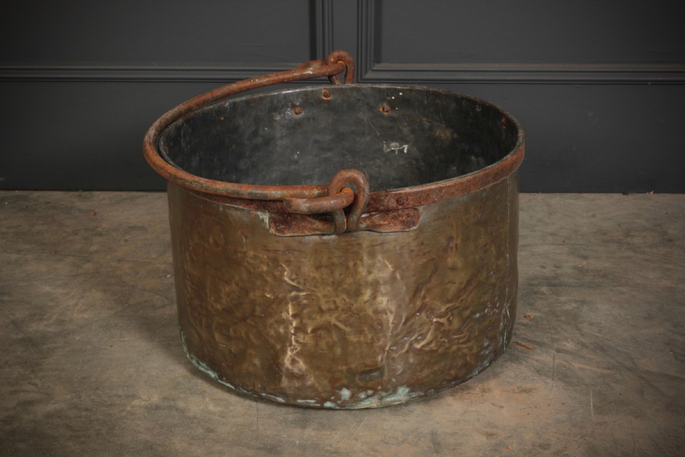 A large, hand-hammered Victorian brass cauldron featuring an iron rim collar and a heavy wrought iron swing handle. View VIII