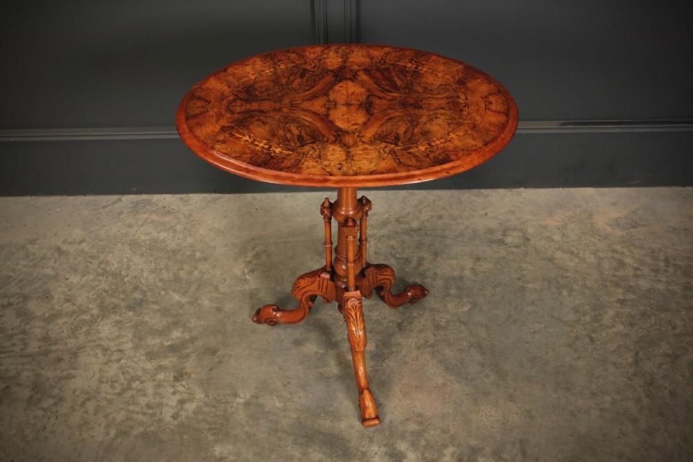 A Victorian oval occasional wine table made from figured walnut featuring floral marquetry inlay and a carved tripod base.