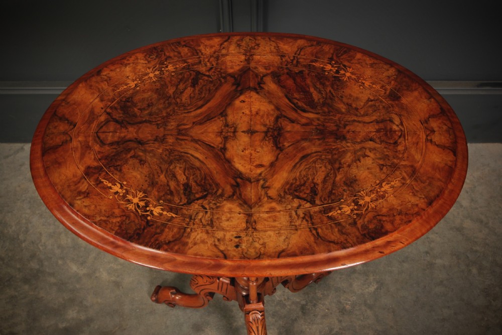A Victorian oval occasional wine table made from figured walnut featuring floral marquetry inlay and a carved tripod base. View IV