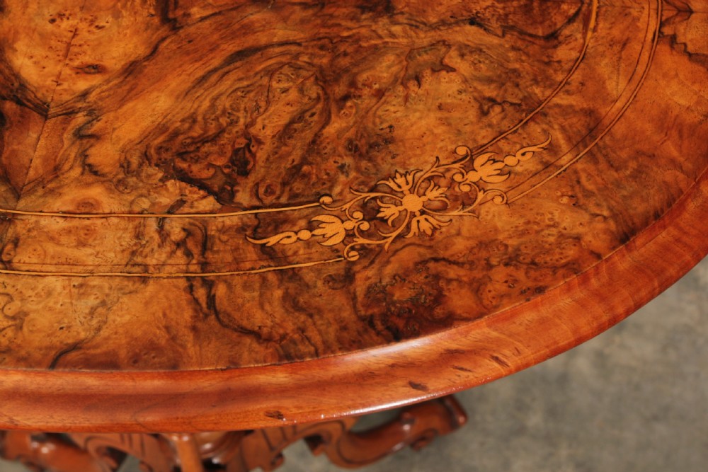 A Victorian oval occasional wine table made from figured walnut featuring floral marquetry inlay and a carved tripod base. View V