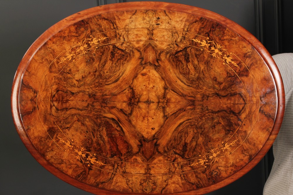 A Victorian oval occasional wine table made from figured walnut featuring floral marquetry inlay and a carved tripod base. View X