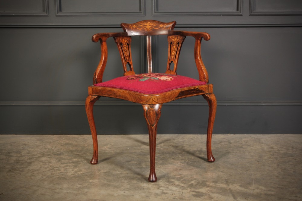 An antique rosewood corner chair featuring floral marquetry inlays on the curved top rail and splats, supported by cabriole legs and upholstered in red floral needlepoint.