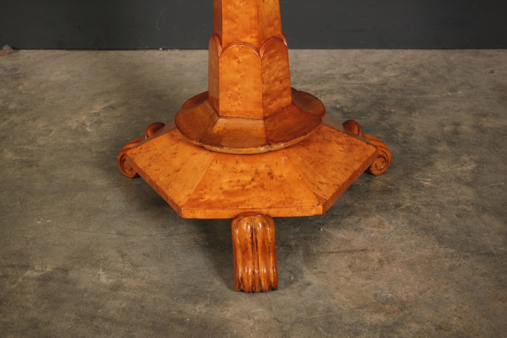 An Art Deco birds eye maple music stool featuring a round cream upholstered swivel seat with brass stud trimming above a faceted pedestal and octagonal base. View IV