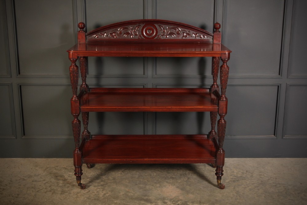 A Victorian mahogany three-tier buffet featuring carved turned column supports, a scrolled decorative backboard, and brass castors. View II