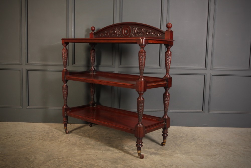 A Victorian mahogany three-tier buffet featuring carved turned column supports, a scrolled decorative backboard, and brass castors. View III