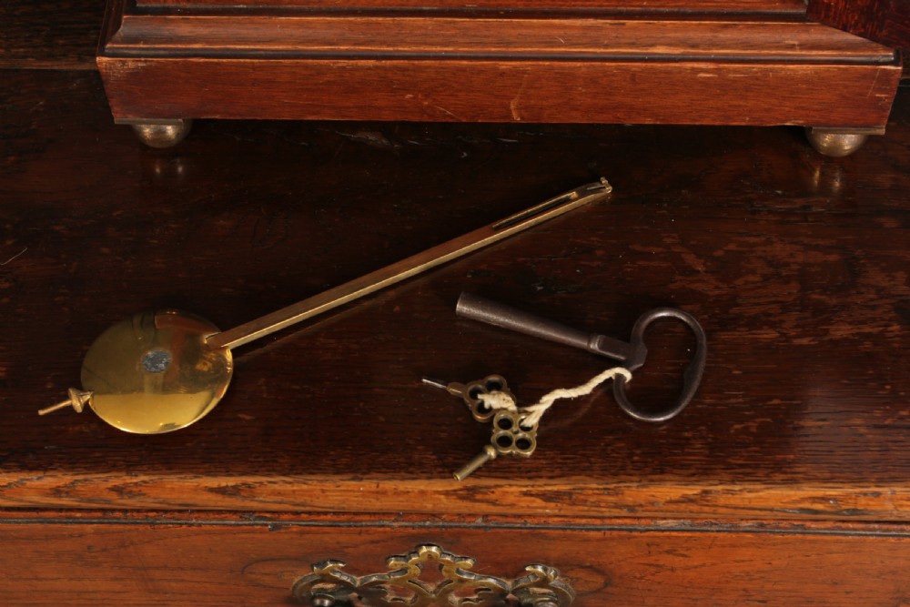 An antique arched mahogany bracket clock featuring brass fretwork panels, a circular dial with Arabic numerals, and small brass ball feet. View VI