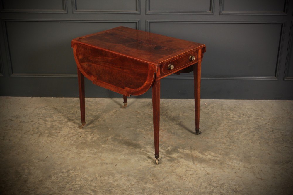 A Georgian mahogany Pembroke table featuring two drop leaves, subtle line inlay, a single front drawer with round brass handles, and tapered square legs on brass castors. View II