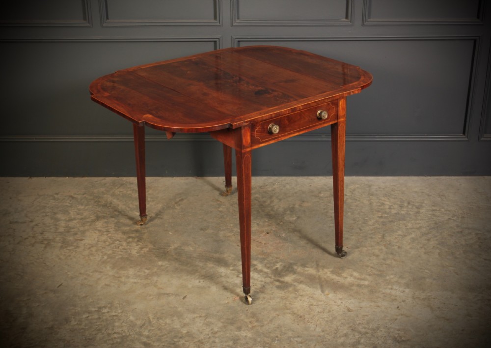 A Georgian mahogany Pembroke table featuring two drop leaves, subtle line inlay, a single front drawer with round brass handles, and tapered square legs on brass castors. View V