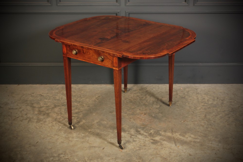 A Georgian mahogany Pembroke table featuring two drop leaves, subtle line inlay, a single front drawer with round brass handles, and tapered square legs on brass castors. View VI