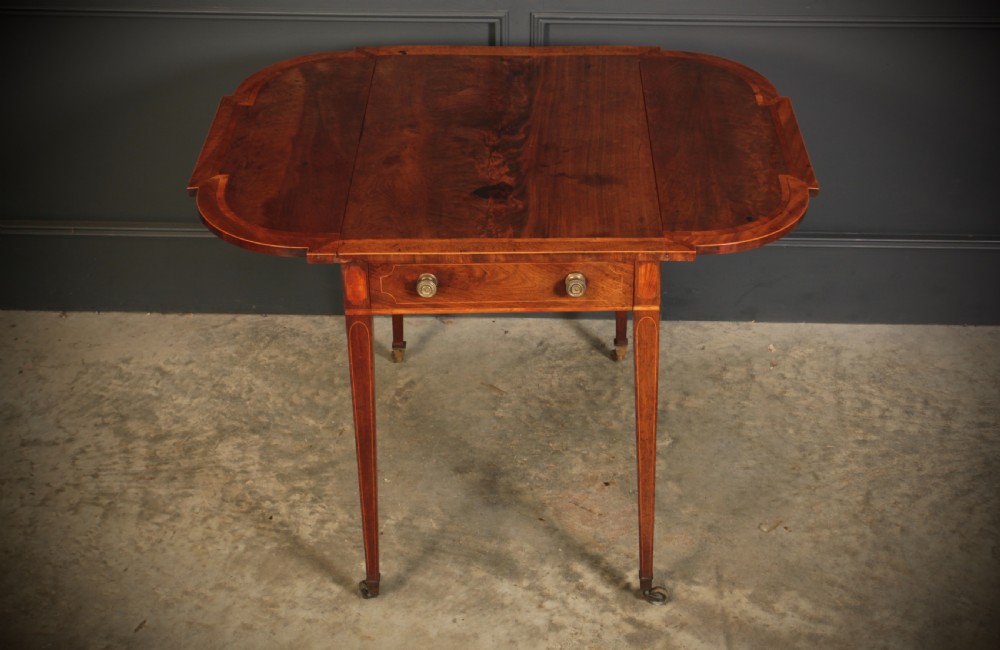 A Georgian mahogany Pembroke table featuring two drop leaves, subtle line inlay, a single front drawer with round brass handles, and tapered square legs on brass castors. View VII