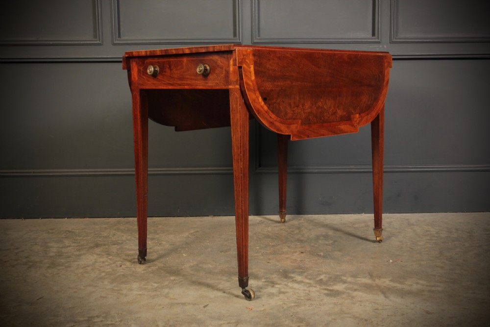 A Georgian mahogany Pembroke table featuring two drop leaves, subtle line inlay, a single front drawer with round brass handles, and tapered square legs on brass castors. View X
