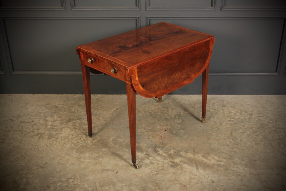 A Georgian mahogany Pembroke table featuring two drop leaves, subtle line inlay, a single front drawer with round brass handles, and tapered square legs on brass castors. View XI