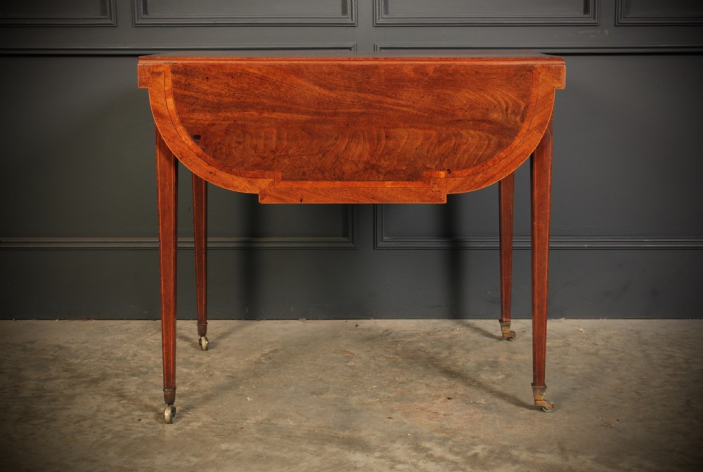A Georgian mahogany Pembroke table featuring two drop leaves, subtle line inlay, a single front drawer with round brass handles, and tapered square legs on brass castors. View XII
