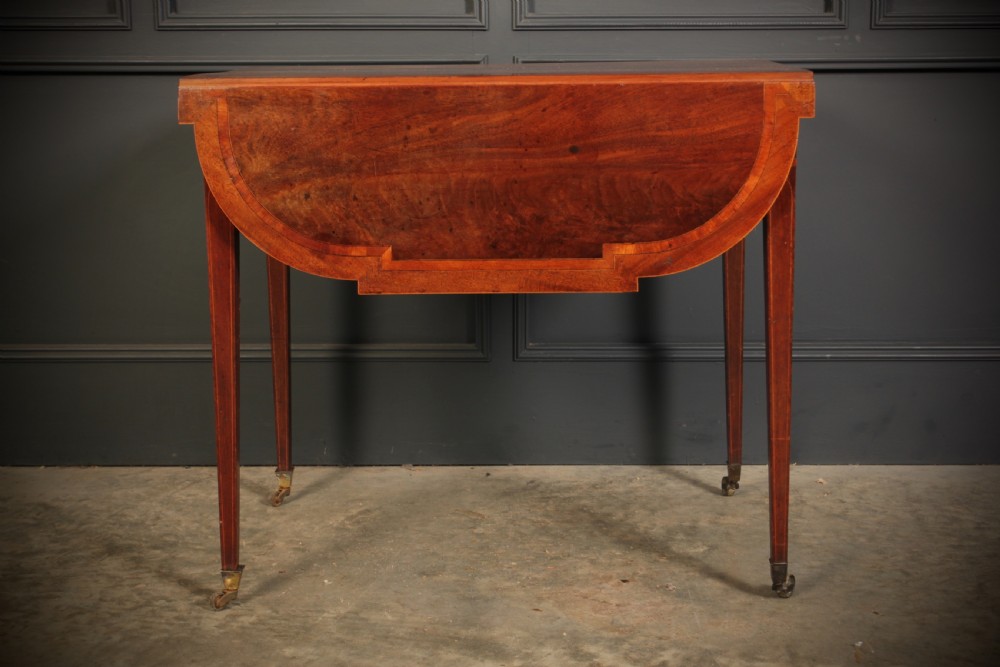 A Georgian mahogany Pembroke table featuring two drop leaves, subtle line inlay, a single front drawer with round brass handles, and tapered square legs on brass castors. View XIV