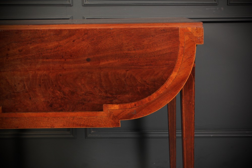 A Georgian mahogany Pembroke table featuring two drop leaves, subtle line inlay, a single front drawer with round brass handles, and tapered square legs on brass castors. View XV