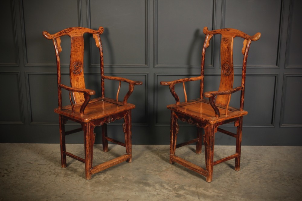 A pair of antique Chinese elm wood armchairs featuring curved yoke-back top rails, carved central back splats, and a warm honey-brown finish.