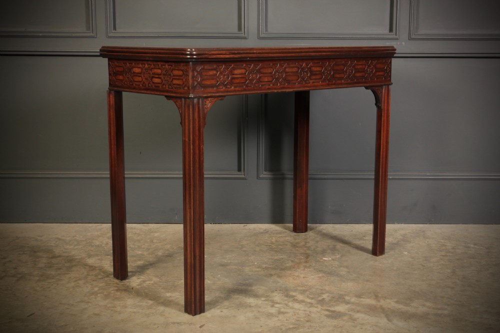 A dark mahogany fold-over card table in the Chinese Chippendale style featuring blind fretwork carved along the frieze and fluted square legs.