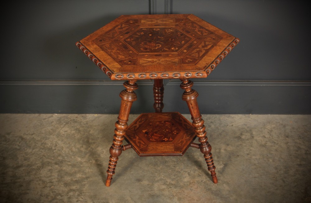 A Victorian hexagonal walnut occasional table featuring floral marquetry inlays, a carved edge, a lower tier, and turned legs.