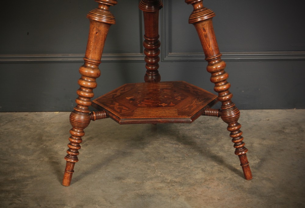 A Victorian hexagonal walnut occasional table featuring floral marquetry inlays, a carved edge, a lower tier, and turned legs. View VI