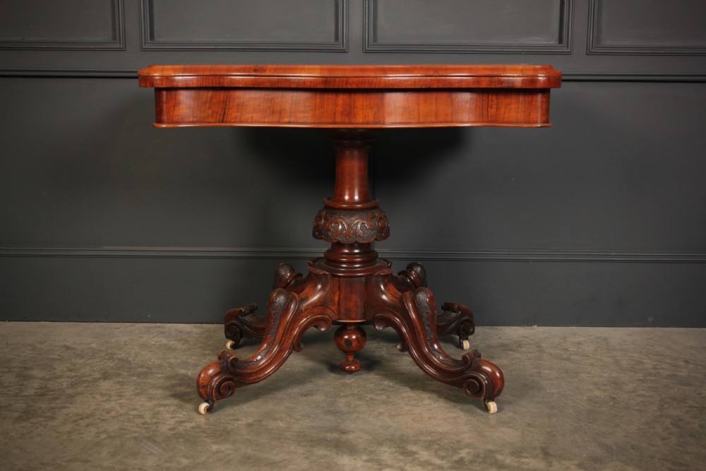 A Victorian figured walnut card table featuring floral marquetry inlay on a serpentine fold-over top, supported by a carved central stem and four cabriole legs on castors. View II