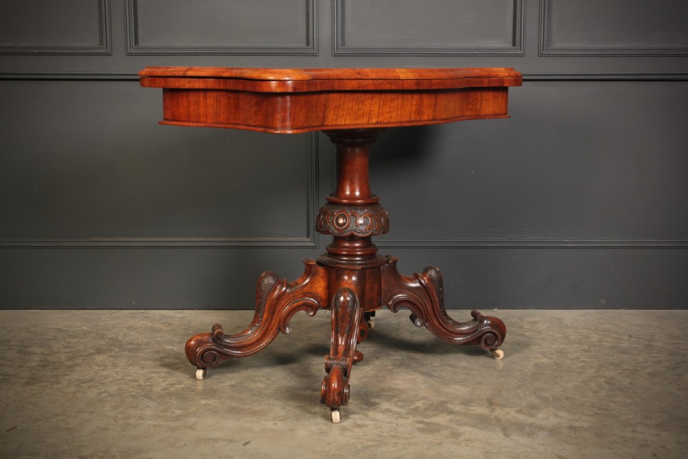A Victorian figured walnut card table featuring floral marquetry inlay on a serpentine fold-over top, supported by a carved central stem and four cabriole legs on castors. View VI