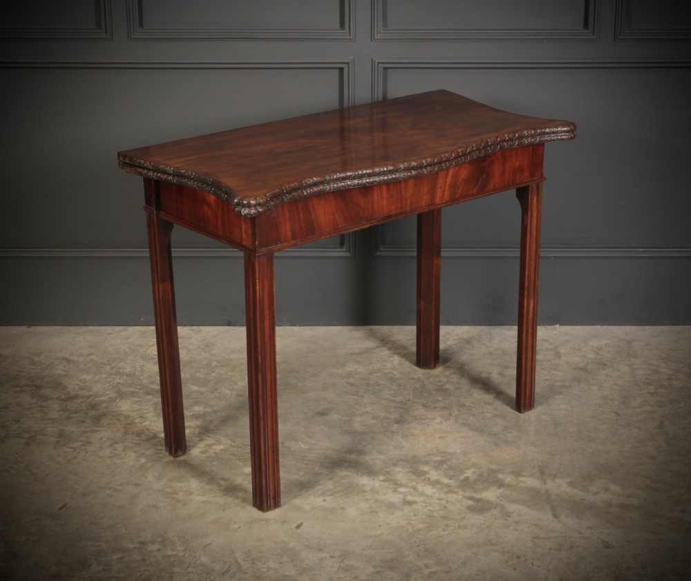 A George IV serpentine mahogany tea table featuring a fold-over top with carved edge moulding and straight fluted legs.