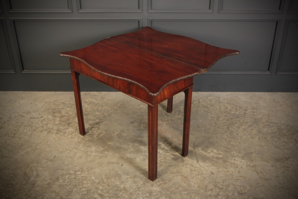 A George IV serpentine mahogany tea table featuring a fold-over top with carved edge moulding and straight fluted legs. View X