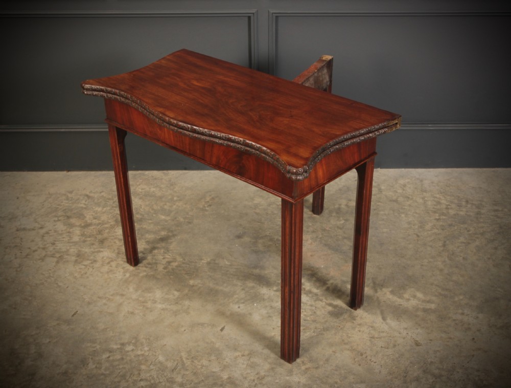 A George IV serpentine mahogany tea table featuring a fold-over top with carved edge moulding and straight fluted legs. View XI