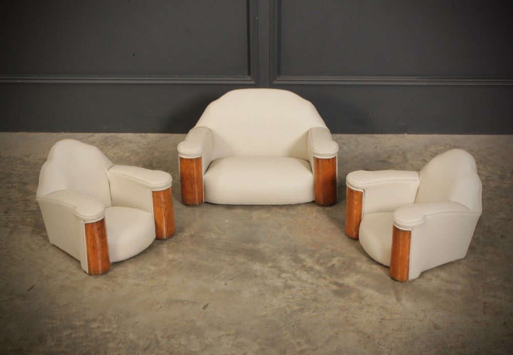 A miniature Art Deco three-piece suite featuring a small sofa and two matching armchairs upholstered in cream leather with polished curved wood arm fronts.