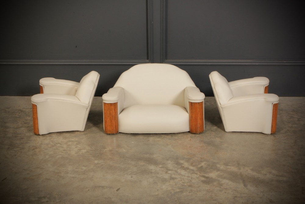 A miniature Art Deco three-piece suite featuring a small sofa and two matching armchairs upholstered in cream leather with polished curved wood arm fronts. View II