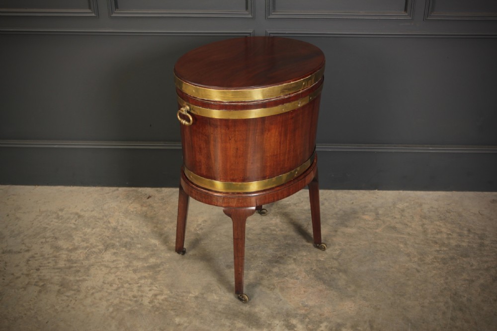 An oval Georgian mahogany wine cooler with brass binding straps, side handles, and tapered square legs on brass castors.
