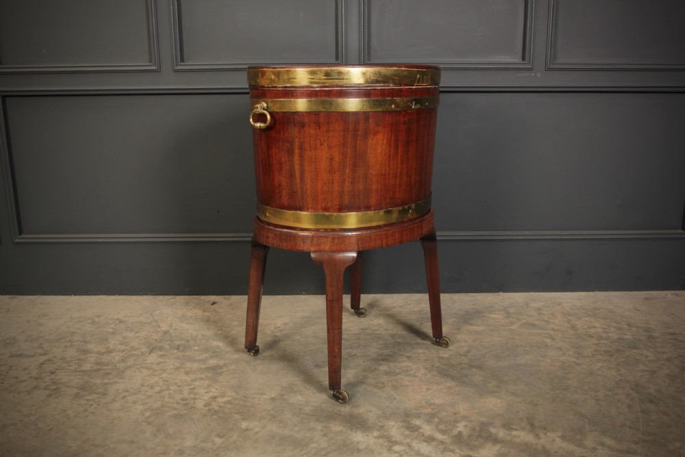 An oval Georgian mahogany wine cooler with brass binding straps, side handles, and tapered square legs on brass castors. View II