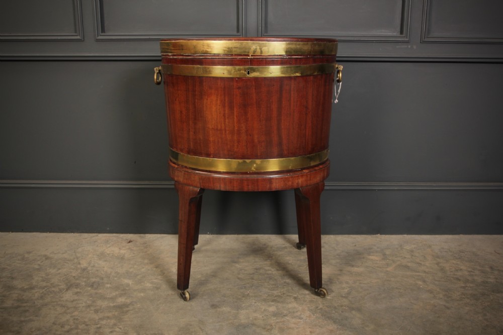 An oval Georgian mahogany wine cooler with brass binding straps, side handles, and tapered square legs on brass castors. View V