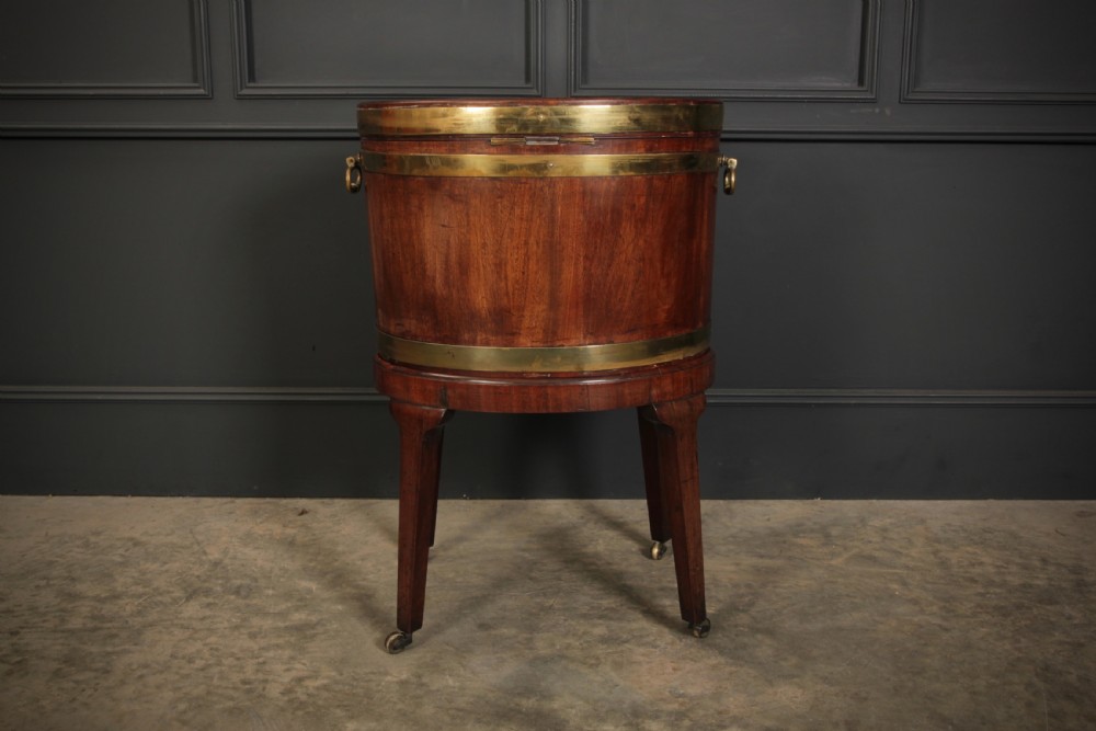 An oval Georgian mahogany wine cooler with brass binding straps, side handles, and tapered square legs on brass castors. View IX