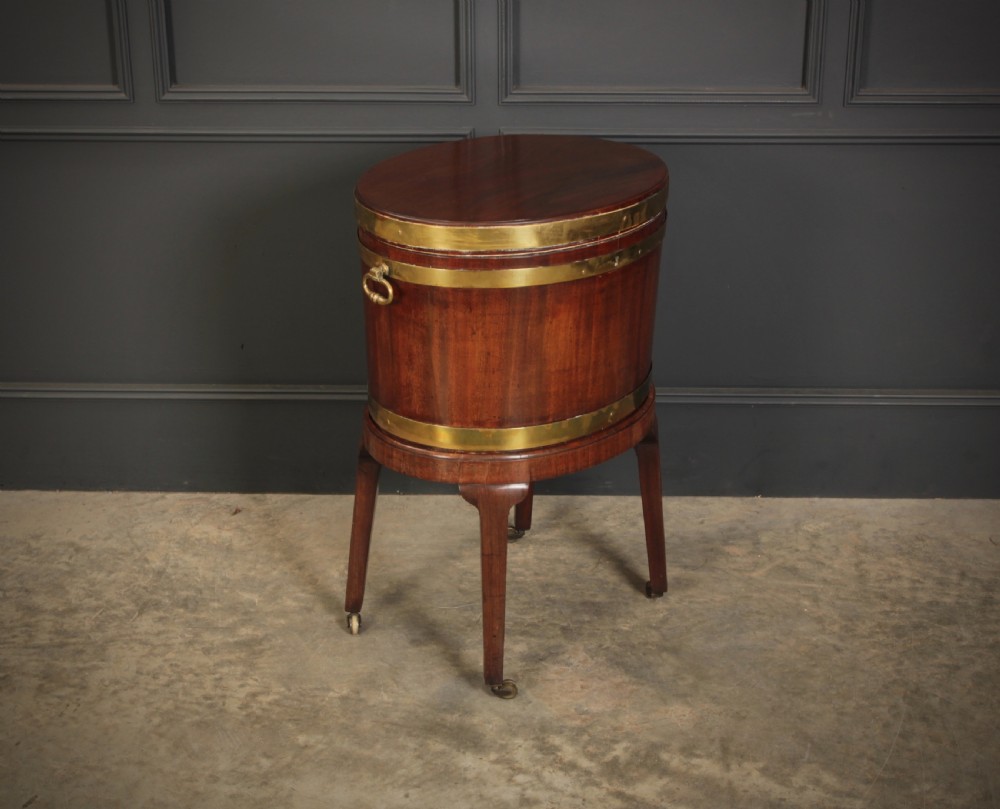 An oval Georgian mahogany wine cooler with brass binding straps, side handles, and tapered square legs on brass castors. View XI