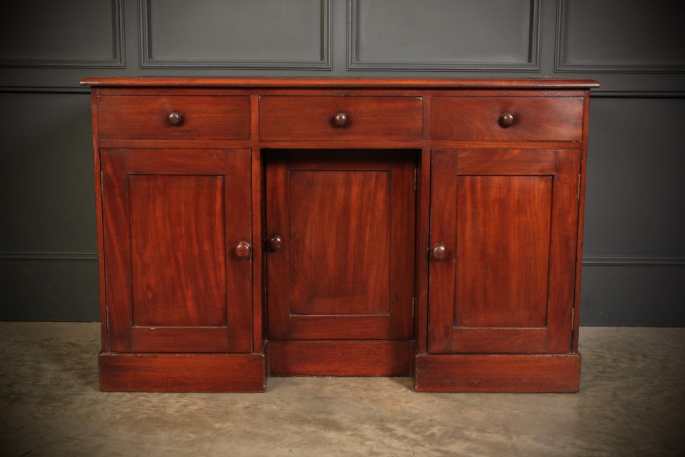 An Early Victorian mahogany kneehole desk with a dark leather writing surface, three frieze drawers, side cupboards, and turned wooden handles. View V