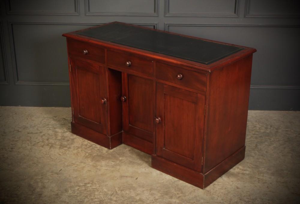 An Early Victorian mahogany kneehole desk with a dark leather writing surface, three frieze drawers, side cupboards, and turned wooden handles. View VII