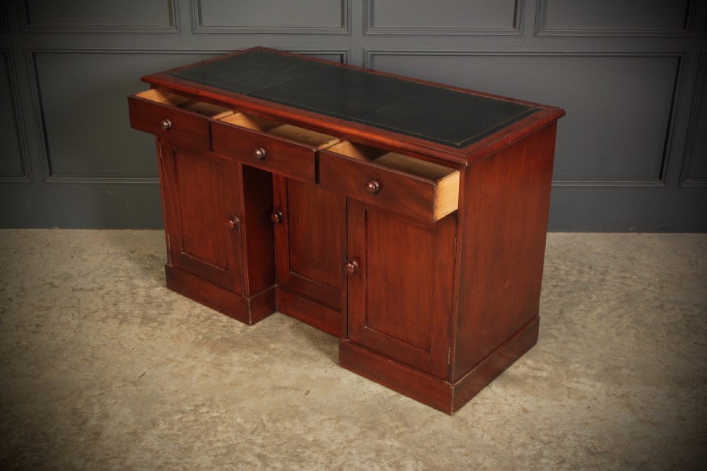 An Early Victorian mahogany kneehole desk with a dark leather writing surface, three frieze drawers, side cupboards, and turned wooden handles. View IX