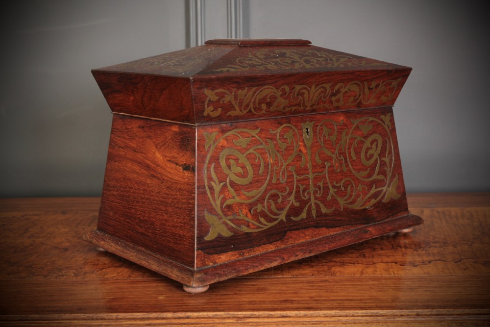 A Regency sarcophagus-form rosewood tea caddy featuring ornate foliate brass inlay across the lid and front panel.