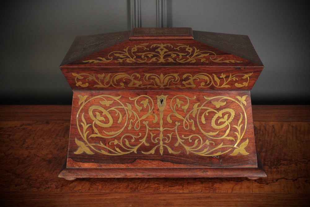 A Regency sarcophagus-form rosewood tea caddy featuring ornate foliate brass inlay across the lid and front panel. View II