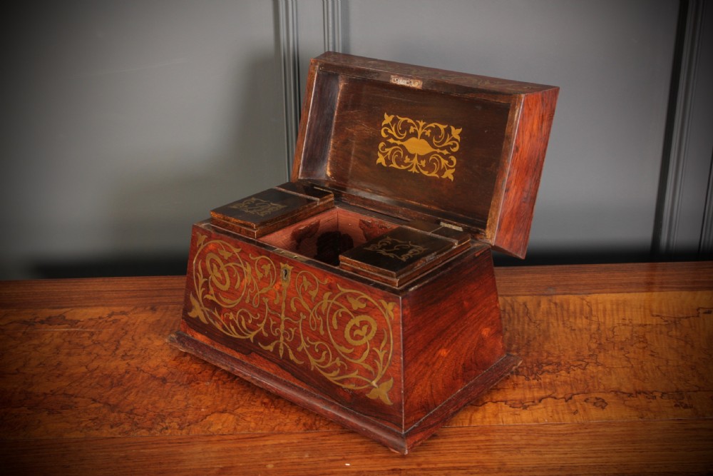 A Regency sarcophagus-form rosewood tea caddy featuring ornate foliate brass inlay across the lid and front panel. View IV