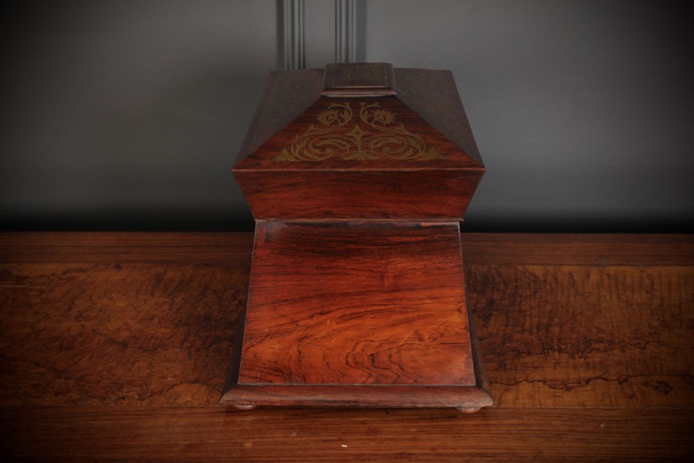 A Regency sarcophagus-form rosewood tea caddy featuring ornate foliate brass inlay across the lid and front panel. View V