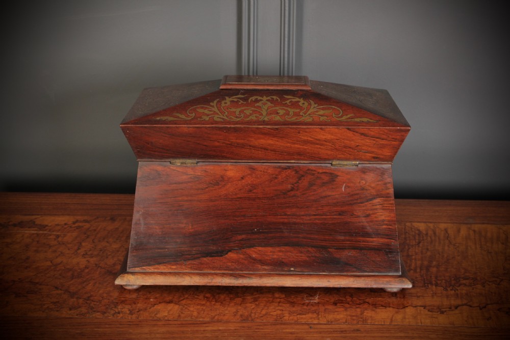 A Regency sarcophagus-form rosewood tea caddy featuring ornate foliate brass inlay across the lid and front panel. View VI
