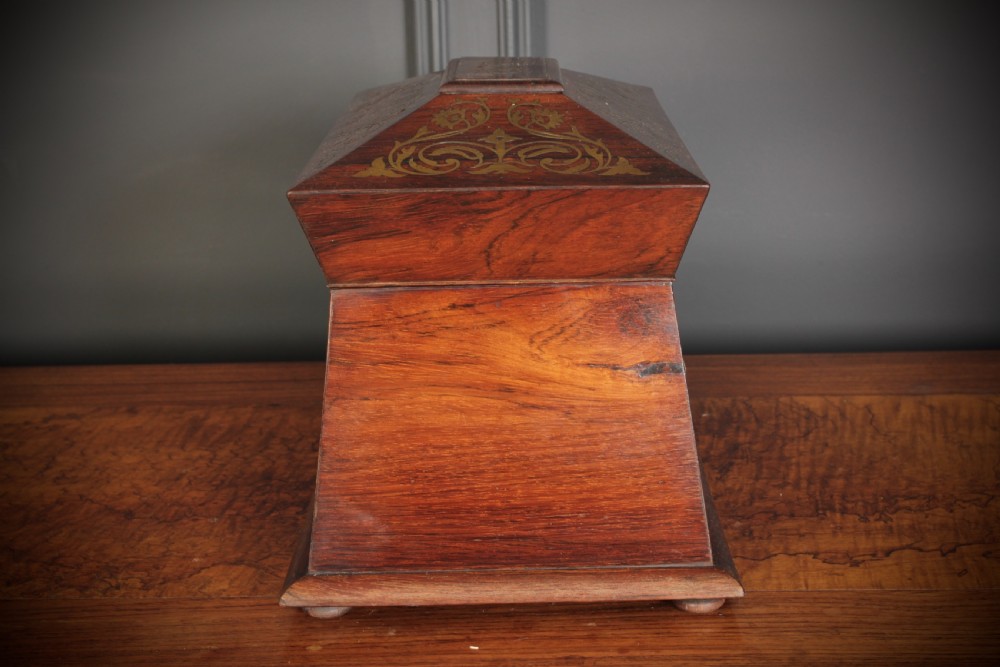 A Regency sarcophagus-form rosewood tea caddy featuring ornate foliate brass inlay across the lid and front panel. View VII