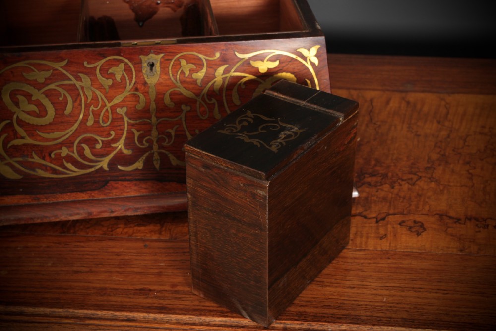 A Regency sarcophagus-form rosewood tea caddy featuring ornate foliate brass inlay across the lid and front panel. View X