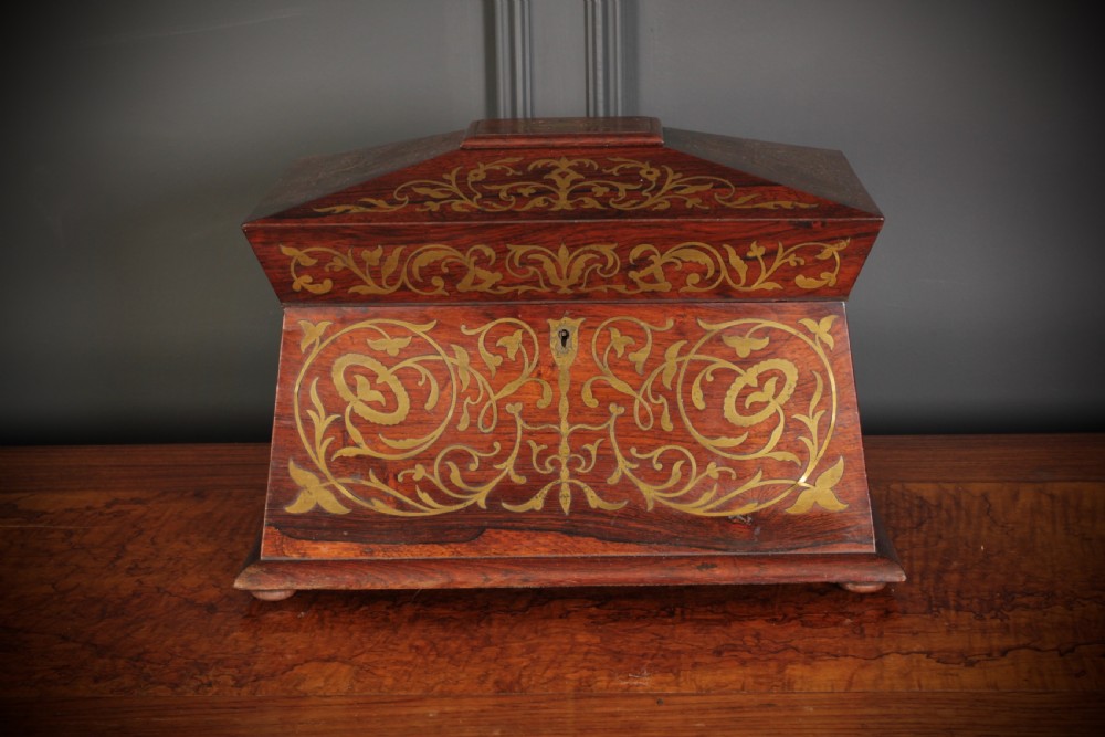 A Regency sarcophagus-form rosewood tea caddy featuring ornate foliate brass inlay across the lid and front panel. View XII