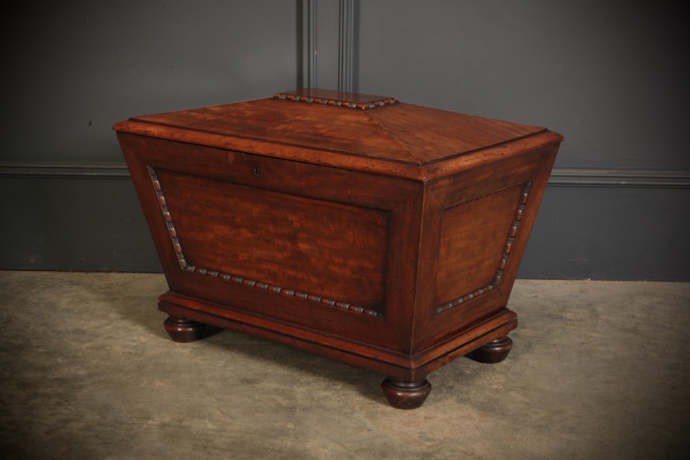 A Regency period mahogany sarcophagus cellarette featuring tapered sides, beaded moulding, and compressed turned feet.