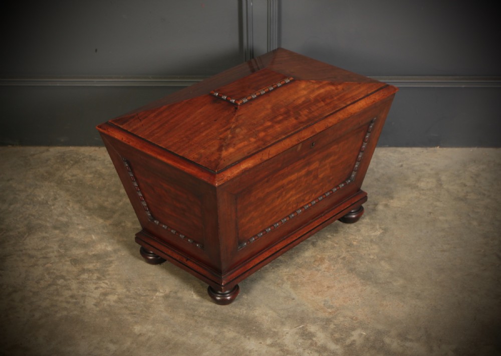 A Regency period mahogany sarcophagus cellarette featuring tapered sides, beaded moulding, and compressed turned feet. View II